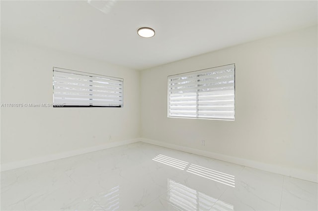 empty room featuring a wealth of natural light, marble finish floor, and baseboards