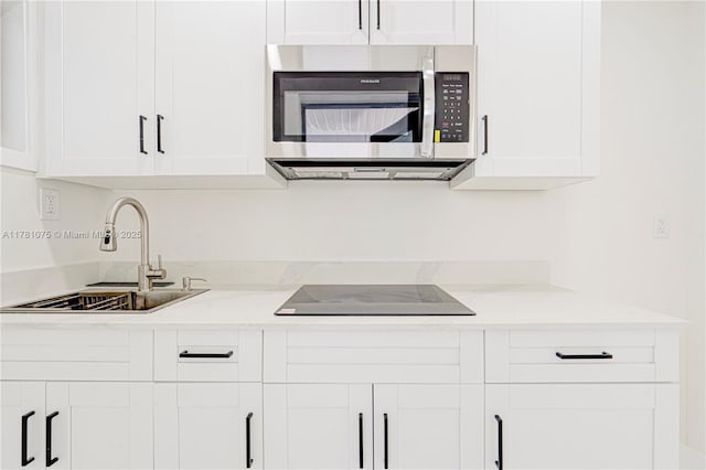 kitchen featuring stainless steel microwave, a sink, white cabinets, and light countertops