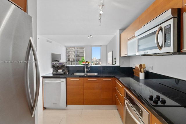 kitchen featuring brown cabinetry, modern cabinets, a sink, light tile patterned floors, and stainless steel appliances