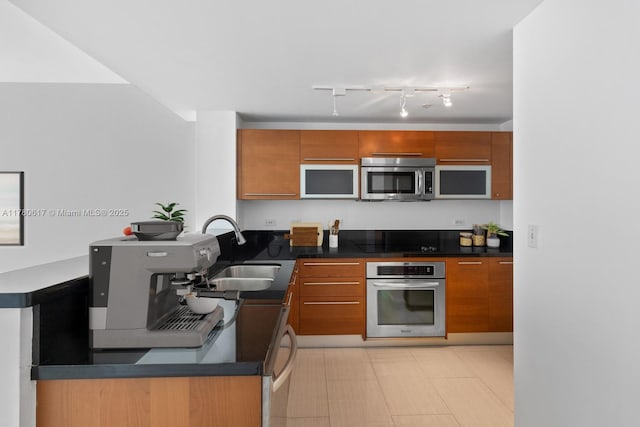 kitchen featuring a sink, appliances with stainless steel finishes, brown cabinetry, and dark countertops