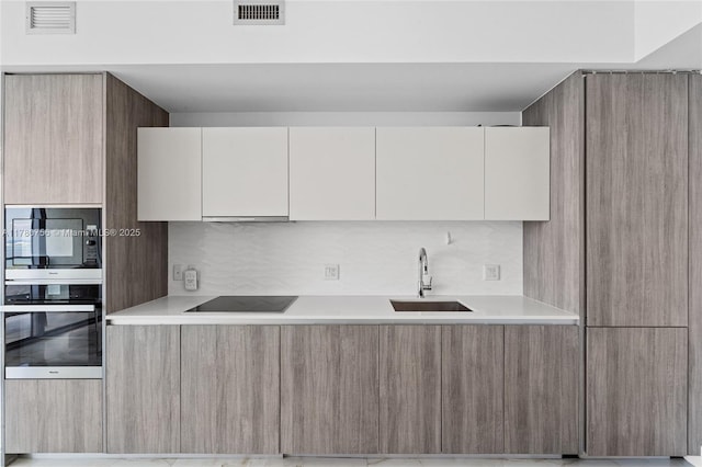 kitchen with stainless steel microwave, oven, black electric cooktop, a sink, and modern cabinets