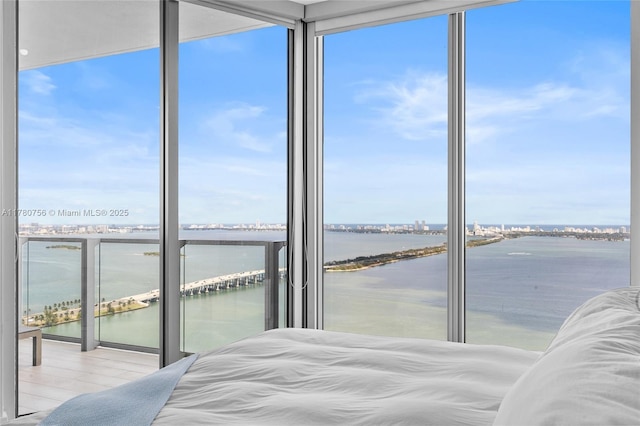bedroom featuring a water view, expansive windows, and wood finished floors