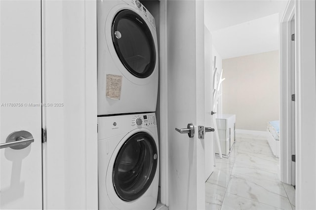 clothes washing area featuring stacked washer and dryer, laundry area, marble finish floor, and baseboards