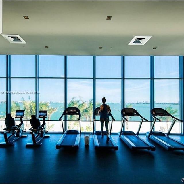 exercise room with a water view, floor to ceiling windows, and visible vents