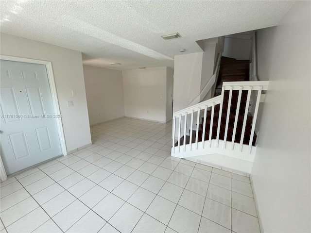 empty room featuring a textured ceiling, light tile patterned flooring, visible vents, and stairs