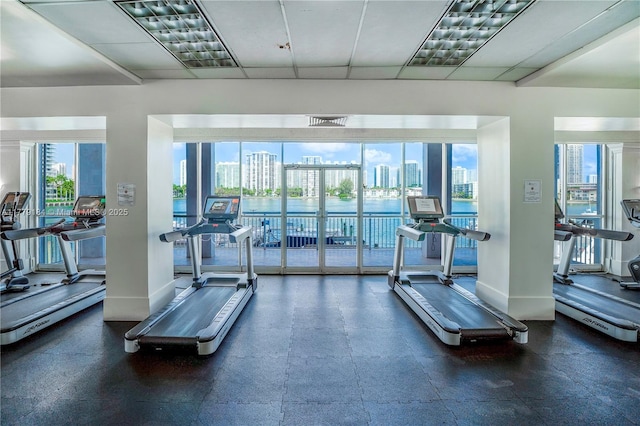 exercise room featuring a view of city, a paneled ceiling, and baseboards