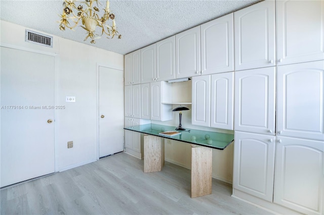 kitchen with a textured ceiling, light wood-style flooring, white cabinets, visible vents, and a chandelier