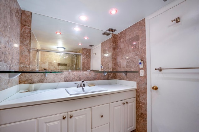 full bath with visible vents, vanity, a shower with door, and tile walls