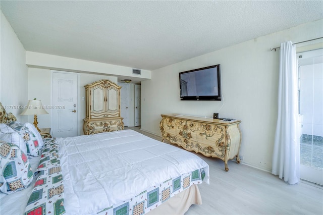bedroom with baseboards, visible vents, wood finished floors, and a textured ceiling