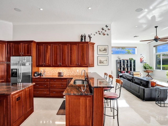 kitchen with stainless steel fridge, a sink, ornamental molding, a kitchen breakfast bar, and a peninsula