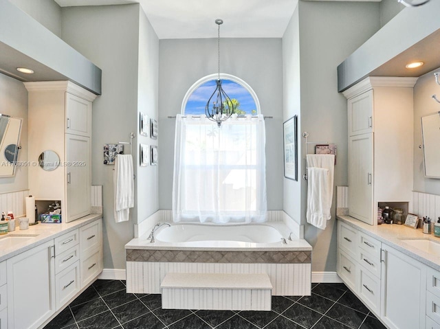 bathroom with a bath, baseboards, a sink, a chandelier, and two vanities
