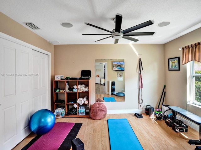workout room with a textured ceiling, a ceiling fan, visible vents, wood finished floors, and baseboards