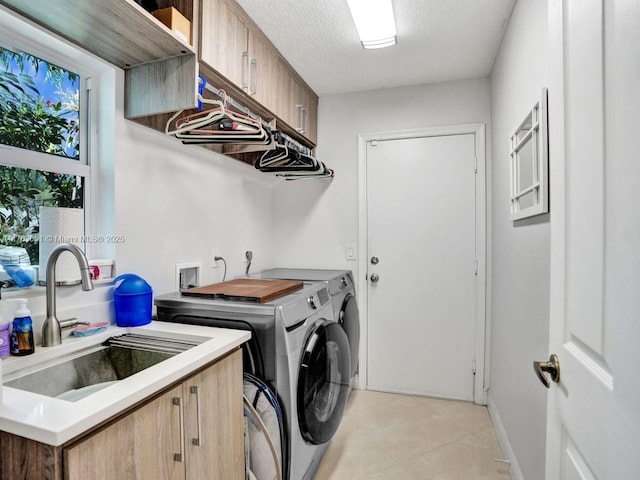 laundry area with light tile patterned floors, washing machine and dryer, a textured ceiling, cabinet space, and a sink