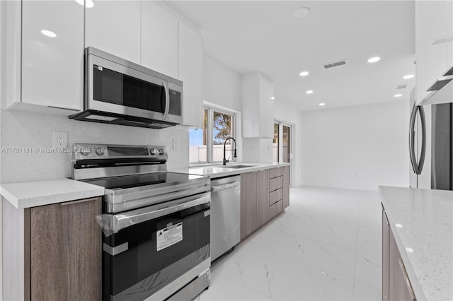kitchen with appliances with stainless steel finishes, a sink, modern cabinets, and white cabinets