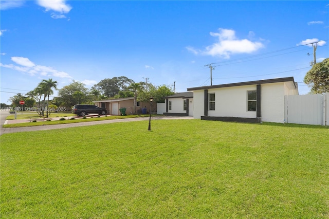 view of front of property with driveway, a front yard, fence, and stucco siding