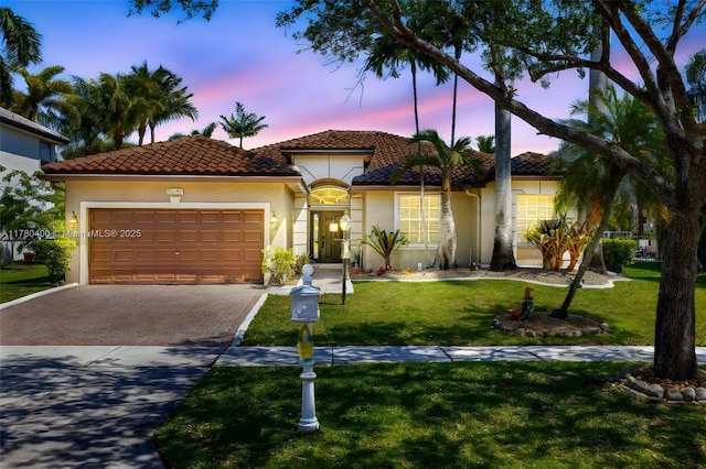 mediterranean / spanish-style house featuring a yard, a tiled roof, an attached garage, stucco siding, and decorative driveway