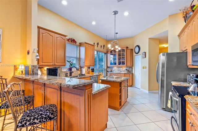 kitchen featuring tasteful backsplash, light stone counters, a peninsula, appliances with stainless steel finishes, and a sink