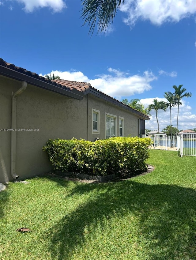 view of property exterior featuring a yard, stucco siding, fence, and a tile roof