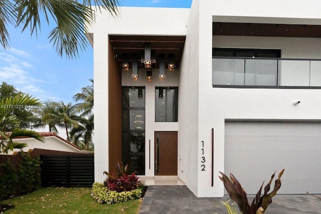 entrance to property with a garage, stucco siding, and fence