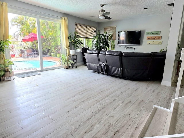 living area featuring visible vents, a textured ceiling, a ceiling fan, and wood finished floors
