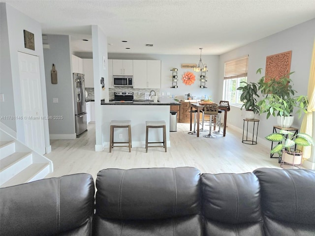 living area featuring stairway, light wood finished floors, a notable chandelier, and baseboards