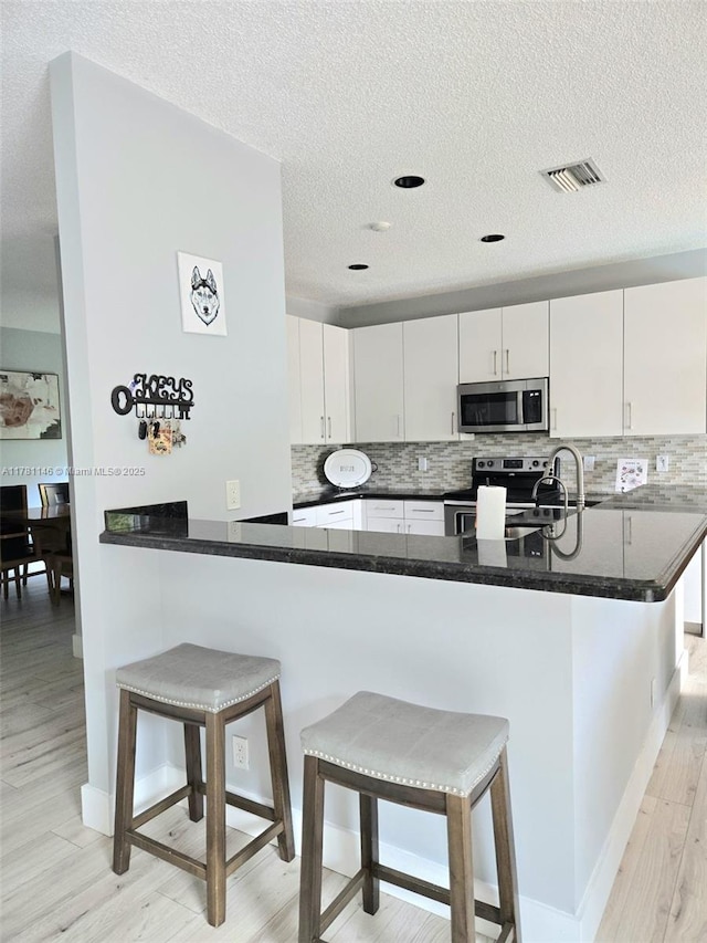 kitchen featuring tasteful backsplash, appliances with stainless steel finishes, light wood finished floors, and a breakfast bar