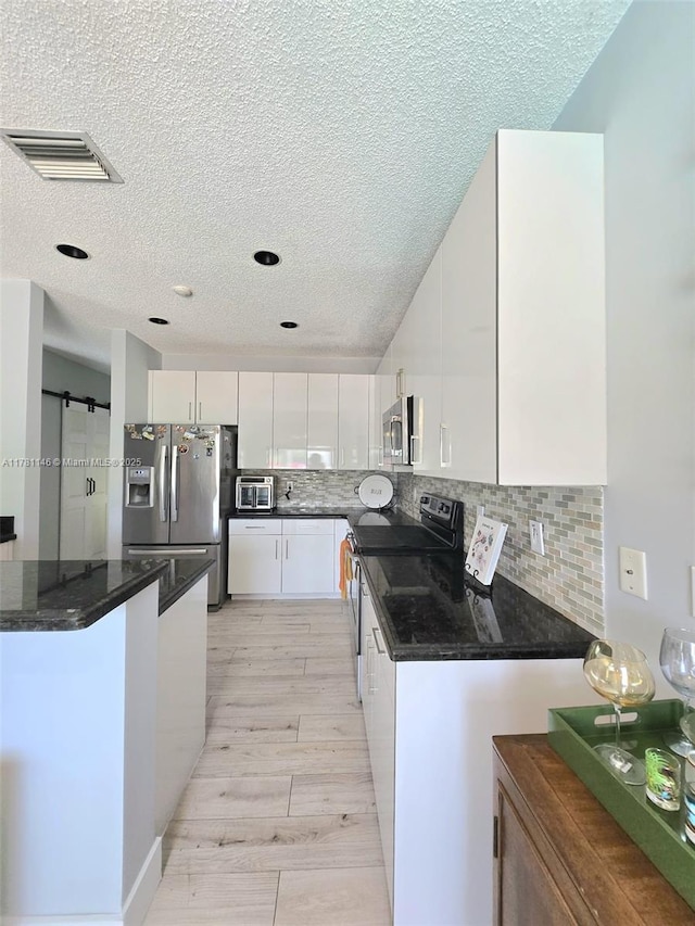 kitchen with a textured ceiling, white cabinetry, visible vents, appliances with stainless steel finishes, and backsplash