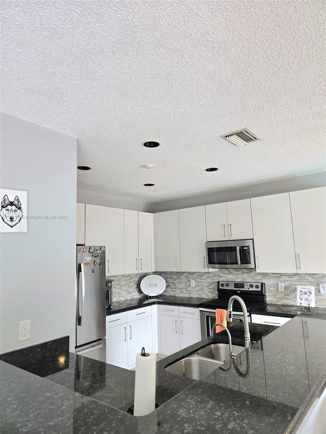 kitchen featuring a textured ceiling, dark stone countertops, appliances with stainless steel finishes, a sink, and backsplash