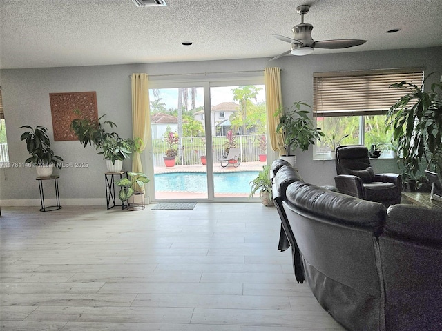 living room with visible vents, baseboards, ceiling fan, a textured ceiling, and wood finished floors