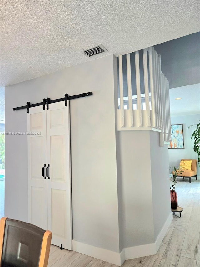 interior space featuring baseboards, a textured ceiling, a barn door, visible vents, and wood finished floors
