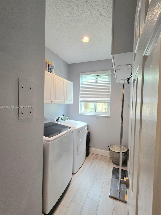laundry area with baseboards, washer and dryer, a textured ceiling, light wood finished floors, and cabinet space