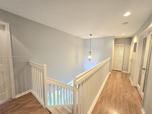 hallway with baseboards, recessed lighting, an upstairs landing, a textured ceiling, and wood finished floors