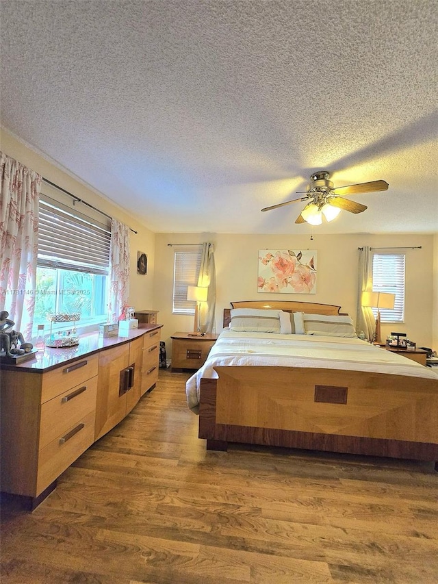 bedroom with dark wood-type flooring, a textured ceiling, a ceiling fan, and multiple windows