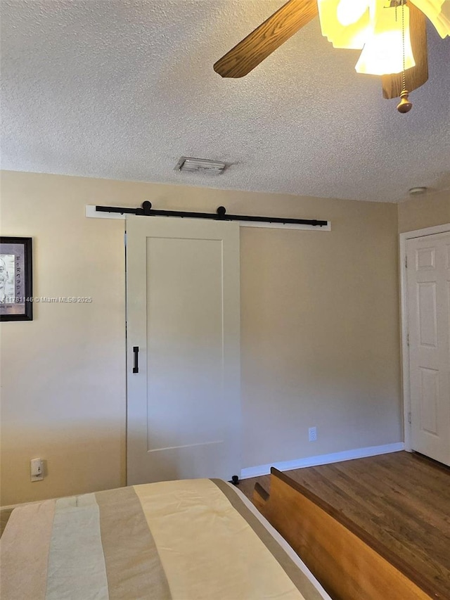 unfurnished bedroom featuring baseboards, a textured ceiling, a barn door, visible vents, and wood finished floors