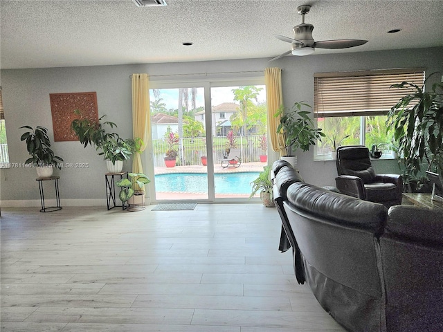 living area with visible vents, baseboards, a ceiling fan, a textured ceiling, and wood finished floors