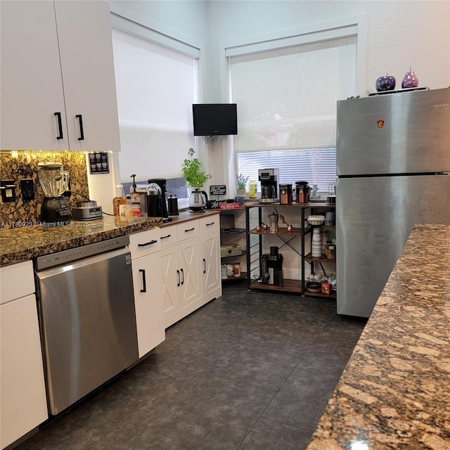 kitchen with white cabinets, dark floors, dark stone countertops, stainless steel appliances, and backsplash