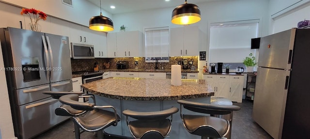 kitchen with white cabinets, a kitchen breakfast bar, stainless steel appliances, decorative backsplash, and finished concrete floors