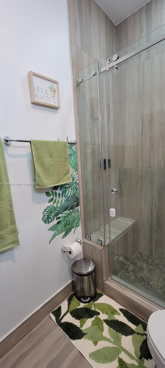 full bathroom featuring baseboards, a stall shower, toilet, and wood finished floors