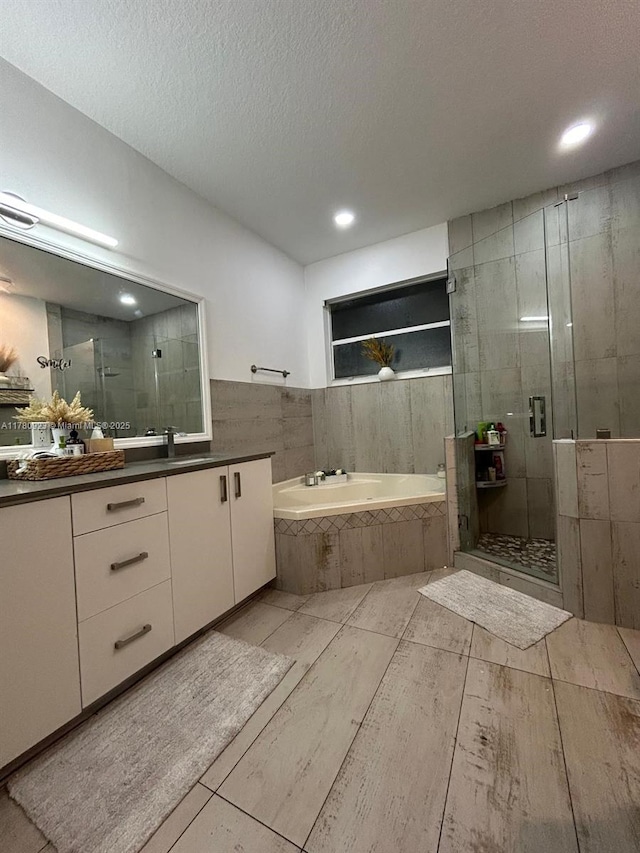 full bathroom featuring a garden tub, vanity, recessed lighting, a textured ceiling, and a shower stall