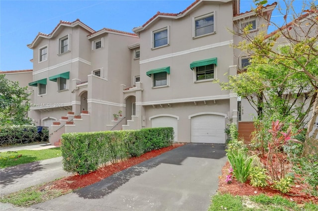 mediterranean / spanish house with a garage, a tiled roof, stucco siding, and aphalt driveway