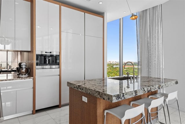 kitchen featuring light stone counters, a kitchen breakfast bar, a sink, marble finish floor, and white cabinetry