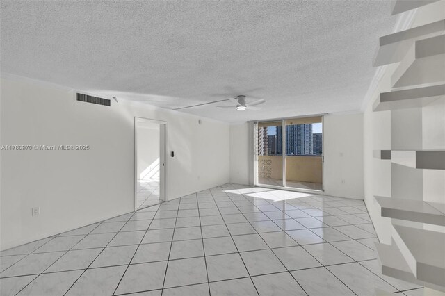 unfurnished room featuring visible vents, light tile patterned floors, a view of city, a ceiling fan, and a textured ceiling