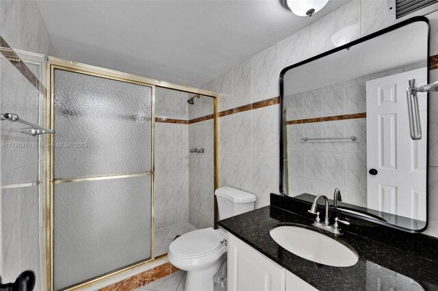 bathroom featuring a shower stall, vanity, tile walls, and toilet