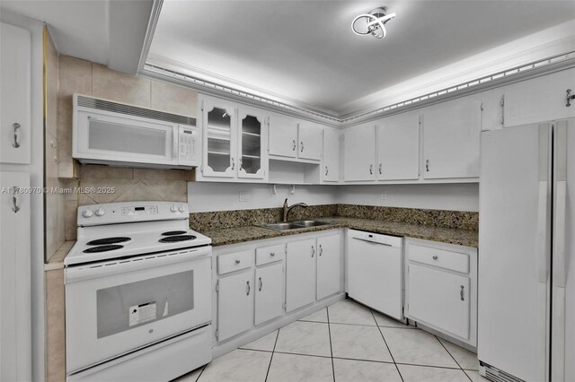 kitchen featuring light tile patterned floors, white appliances, white cabinetry, dark stone countertops, and a sink
