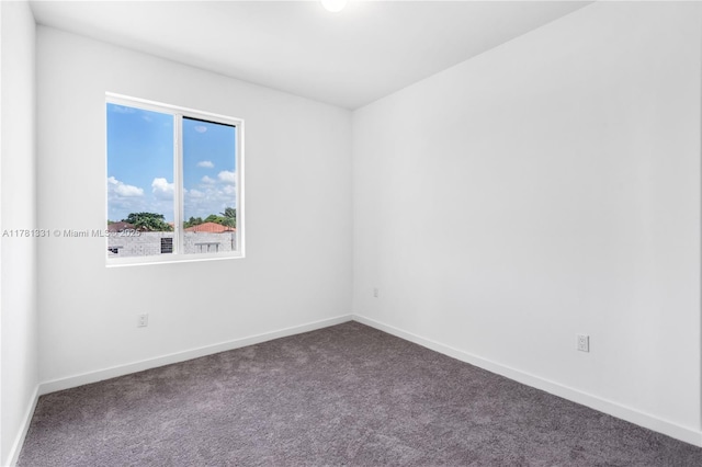spare room featuring dark colored carpet and baseboards