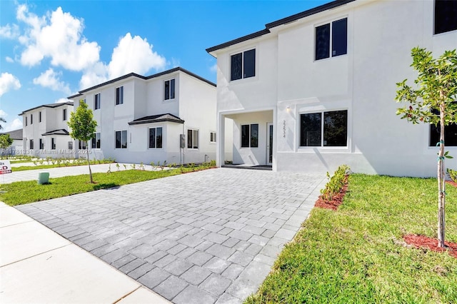 view of front of property with a front lawn, a residential view, decorative driveway, and stucco siding