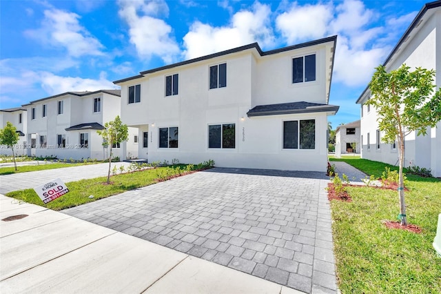 view of front of property with a front yard, a residential view, stucco siding, and decorative driveway