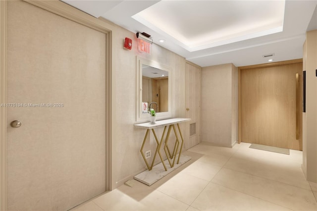 hall featuring a raised ceiling, light tile patterned flooring, and visible vents