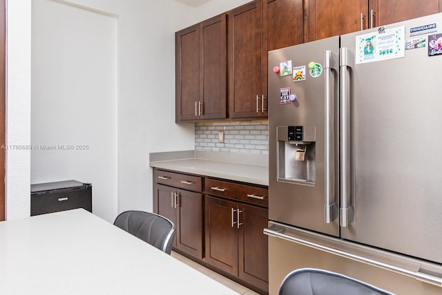 kitchen featuring tasteful backsplash, light countertops, dark brown cabinets, and stainless steel refrigerator with ice dispenser