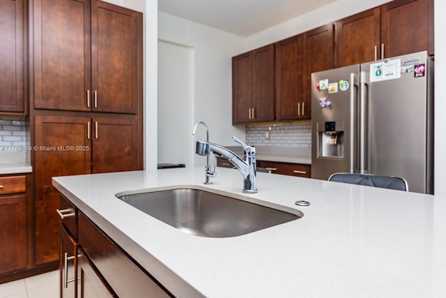 kitchen with tasteful backsplash, stainless steel fridge, light tile patterned floors, light countertops, and a sink